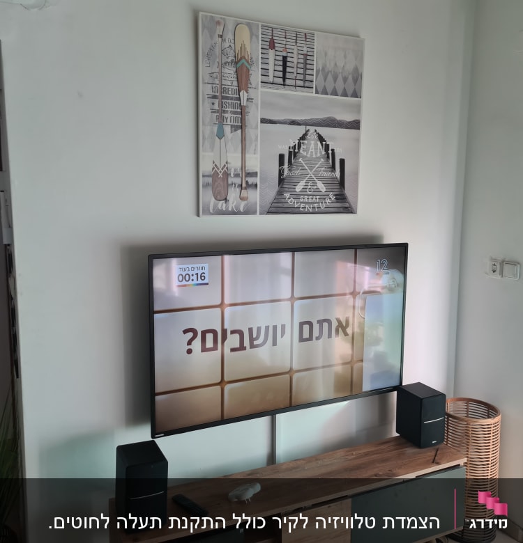 טלוויזיה על קיר עם רמקולים ושלט על מדף